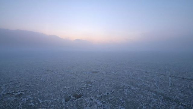 Frozen sea stretching toward misty horizon with cracked ice, ridges and pale sun glow
