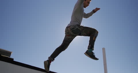 Depicts a man performing parkour on a city rooftop on a sunny day. Demonstrates skill in urban exploration, highlighting agility and athleticism. Ideal for use in articles or advertisements focused on fitness, endurance sports, or urban adventures.