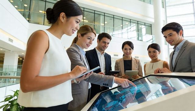 Diverse business team collaborating around interactive touchscreen table in modern atrium