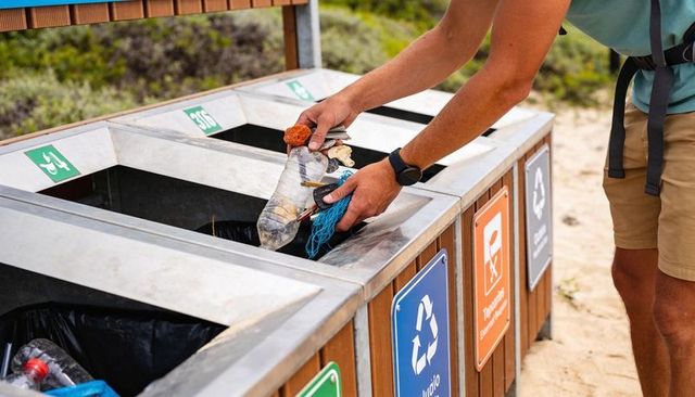Volunteer cleaning beach depositing plastic bottle and fishing line into recycling bins