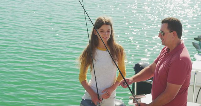 Happy caucasian father teaching teenage daughter fishing, standing on jetty with rods on a sunny day. Leisure, free time, hobbies, family, travel and vacations.