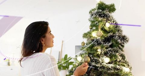 Woman decorating minimal christmas tree with gold baubles and frosted tips cozy interior