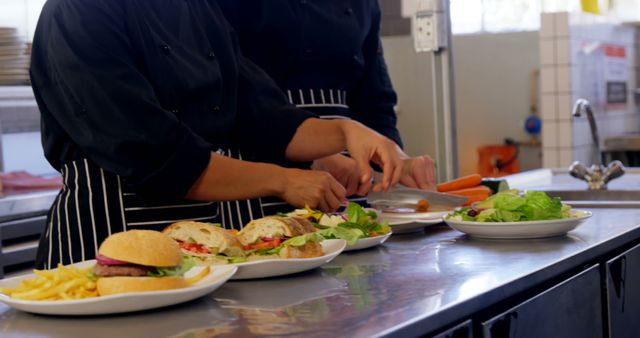 Chefs wearing black uniforms preparing sandwiches and salads in a professional kitchen. This image can be used for culinary-related content, restaurant promotions, food blogs, or cooking class advertisements.