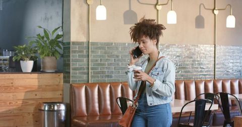 Young african american woman talking on phone holding coffee in trendy cafe