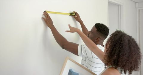 Couple planning wall decor using measuring tape