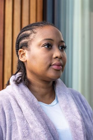 African american woman standing on porch wearing lavender robe, cornrows and nose ring