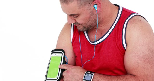 Man interacting with smartphone secured in arm band, wearing earbuds. Ideal for fitness, exercise, and tech-related promotions or advertisements showcasing fitness accessories, apps, or workout gear.