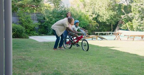 Father teaching child to ride bicycle in sunny backyard