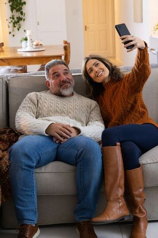 Couple taking selfie on light-gray sofa wearing knit sweaters and leather boots