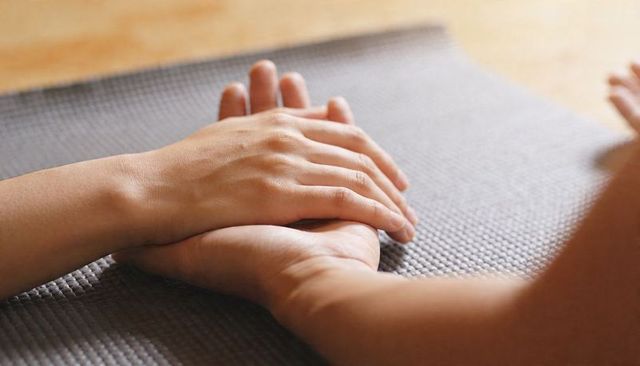 Holding hands on yoga mat conveying gentle support calm and mindful wellness care