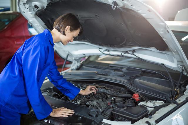 Female mechanic examining engine in repair garage, showcasing women in automotive industry, ideal for articles on gender diversity in trades, automotive service promotions, and educational materials on car maintenance.