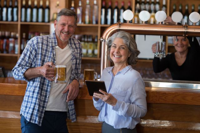 Smiling friends using digital tablet while having glass of beer at counter in bar