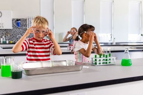 Elementary students wearing safety goggles conducting green liquid chemistry experiments