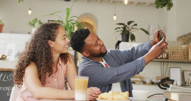 Young couple smiling and taking selfie in cozy cafe. Perfect for concepts of happy relationships, social media interaction, and relaxation. Ideal for promotions of cafes, coffee brands, or lifestyle content involving modern technology and togetherness.