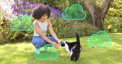 Smiling woman petting black and white cat on sunlit lawn with holographic cloud icons