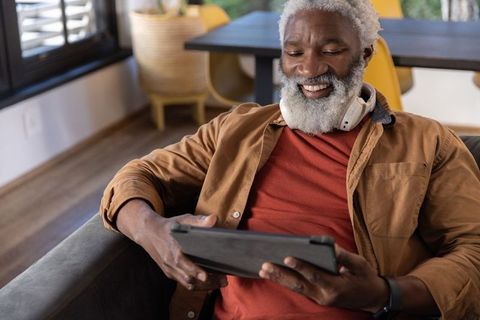 Senior african american man relaxing on sofa smiling and browsing tablet with headphones