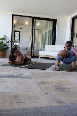 African american family doing yoga on patio — parents planking while child climbs