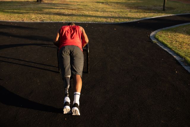 This image captures a determined man with a prosthetic leg performing push ups at an outdoor gym in a park. Ideal for content related to fitness, disability, motivation, and healthy living. Can be used for blogs, fitness inspiration, health-related articles, and promotional material for gyms or fitness programs.