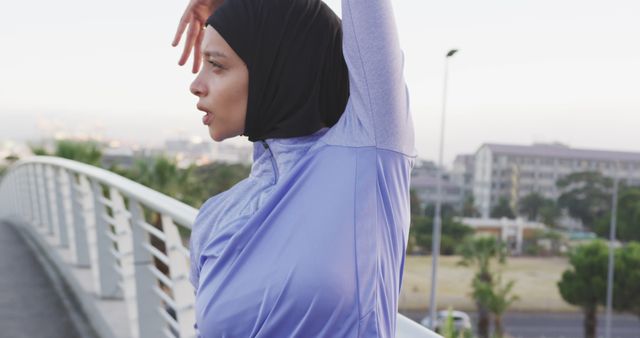 Woman wearing sports hijab stretching and preparing for a workout session outdoors. This can be used for content promoting fitness, wellness, and inclusive sportswear. Suitable for advertisements, articles, and social media posts related to healthy lifestyle and active living.