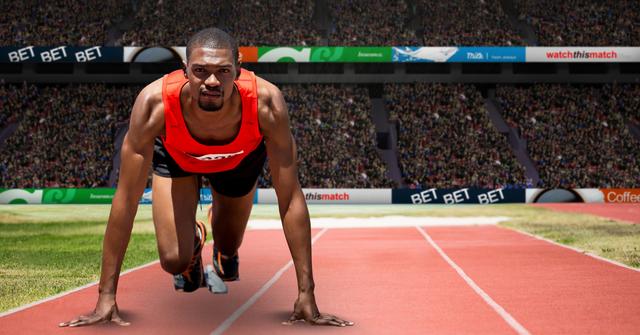 A male sprinter is on the starting line of a track, preparing to race in a large stadium filled with spectators. His expression shows focus and determination, reflecting his readiness for the competition. Use this for sports events promotion, athletic wear advertisements, articles on competition preparedness, or marketing materials emphasizing speed and performance.