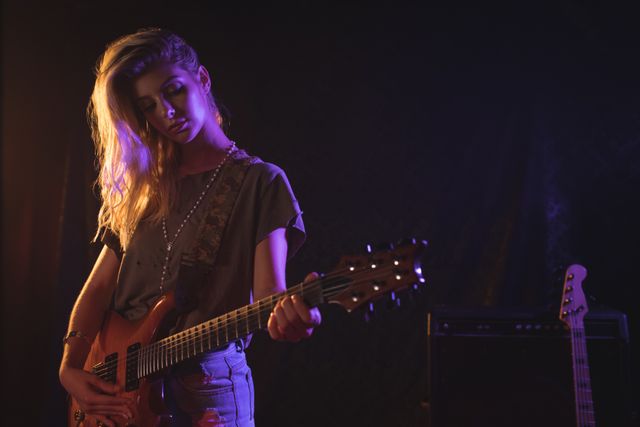 Young female guitarist passionately playing electric guitar on stage during a live concert. Ideal for use in music-related promotions, concert advertisements, artist profiles, and entertainment industry content.