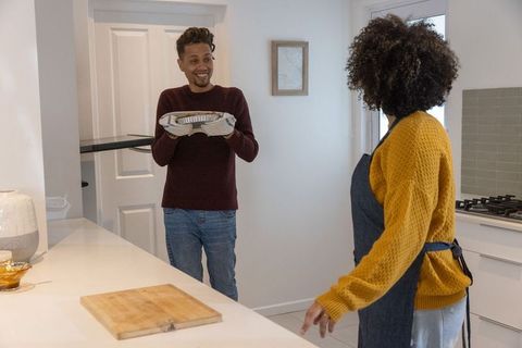 African american couple sharing home-cooked meal, smiling while serving foil tray in modern kitchen