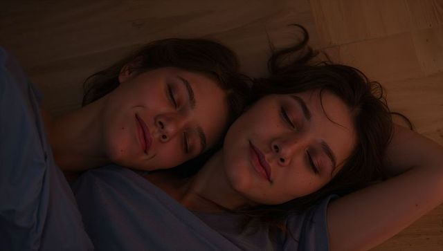 Two women resting on hardwood floor in soft warm light, sharing calm intimacy
