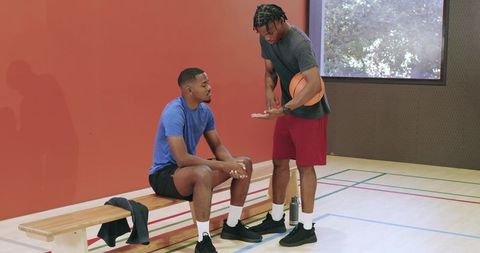 Basketball coach demonstrating footwork and counting steps to player on court bench
