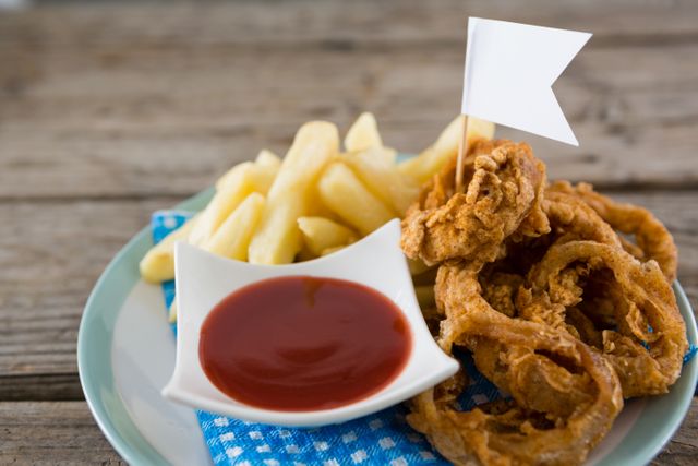 Crispy onion rings and French fries served on a plate with a side of ketchup on a rustic wooden table. Ideal for use in food blogs, restaurant menus, fast food advertisements, or social media posts about comfort food and snacks.