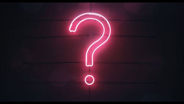 Neon pink question mark sign on dark wall at night