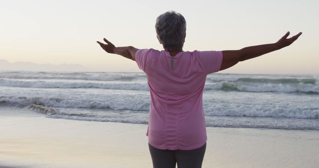Rear view of african american senior woman with arms wide open standing on the beach. retirement active senior lifestyle.