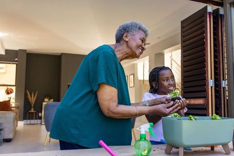 African grandmother guiding granddaughter planting seedlings in indoor planter by folding doors