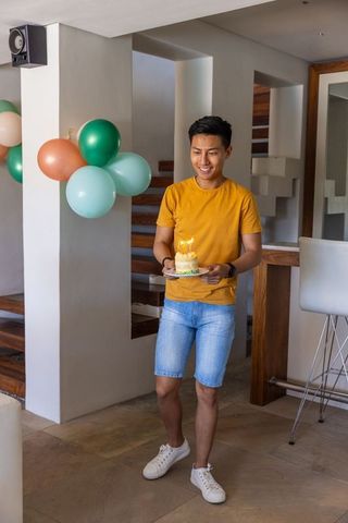 Man celebrating birthday at home holding cake with lit candles and balloons