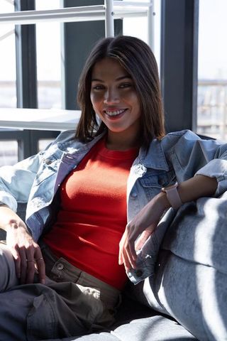 Smiling asian woman relaxing on modern sofa wearing denim jacket and red knit top