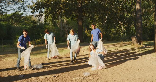 Group of young volunteers cleaning litter in park during daytime. They are picking up trash and placing it in bags, showcasing teamwork and community service efforts. Ideal for campaigns promoting environmental protection, community involvement, and green initiatives. Great for illustrating service projects, volunteerism, and efforts to maintain cleaner public spaces.