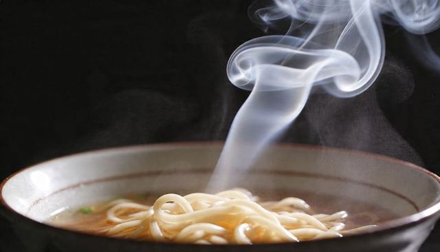 Steaming udon noodles in ceramic bowl with rich broth and rising smoke