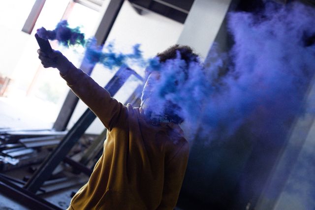 African american transgender woman holding a blue smoke grenade in empty parking garage. concept of gender expression, identity and diversity.