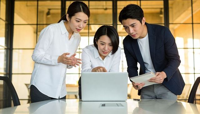 Collaborating business team brainstorming around laptop in modern open office workspace