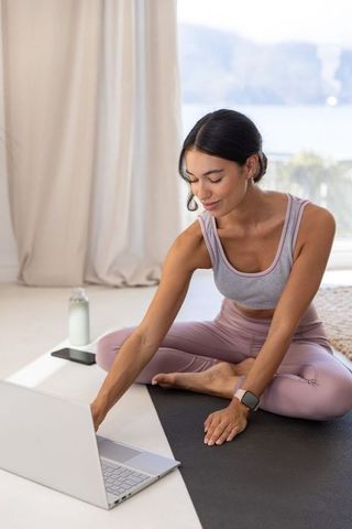 White woman practicing yoga at home checking laptop with water bottle wearing smartwatch