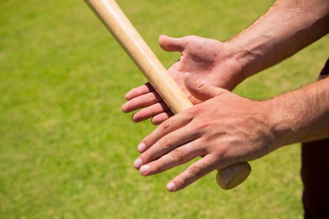 Close-up view of a player's hands gripping a baseball bat on a grassy field. Ideal for use in sports-related content, articles on baseball techniques, athletic training materials, or promotional materials for baseball events.