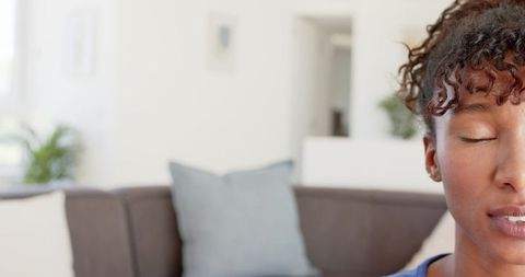 African american woman meditating on sofa in blue top with natural light and calm face