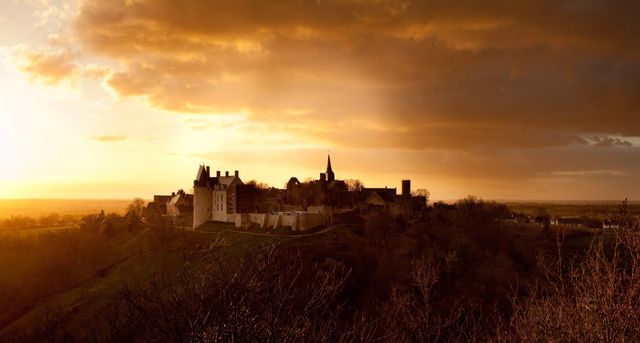 Medieval castle standing atop a hill, bathed in golden sunset light. Silhouetted structure against the warm hues of the evening sky. Perfect for travel brochures, historical publications, and scenic postcards. Evokes a sense of mystery and historical significance. Ideal for promoting tourism in historical regions.