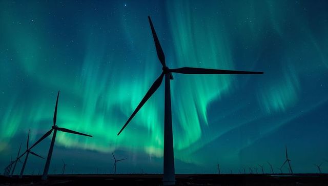 Towering wind turbine silhouettes under vibrant aurora borealis over flat wind farm nightscape