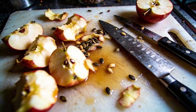 Rustic apple cores and knives on juice-stained cutting board with seeds and peels