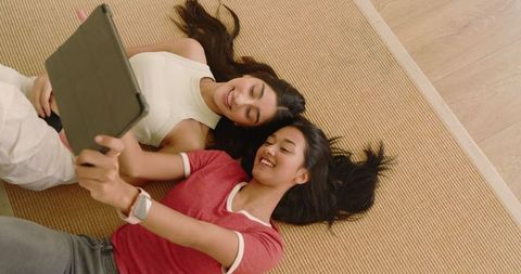 Female friends relax relaxing with tablet on woven rug