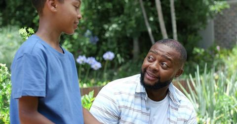 African american father smiling and listening to son on garden bench sharing conversation