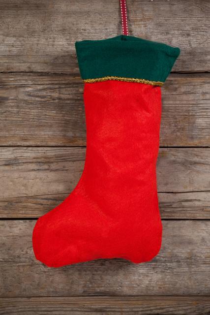 Red Christmas stocking with green trim hanging on rustic wooden wall. Perfect for holiday-themed designs, Christmas cards, festive advertisements, and seasonal blog posts. Ideal for conveying a traditional and cozy holiday atmosphere.