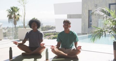 Meditating men on sunny poolside terrace with ocean view practicing yoga and mindfulness