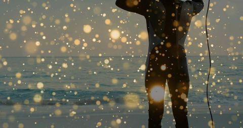 Silhouetted surfer awaiting waves at golden hour with glowing bokeh and ocean horizon