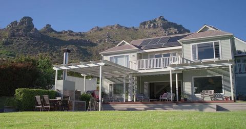 Light-gray two-story house featuring solar panels, wooden deck, pergola, mountain view